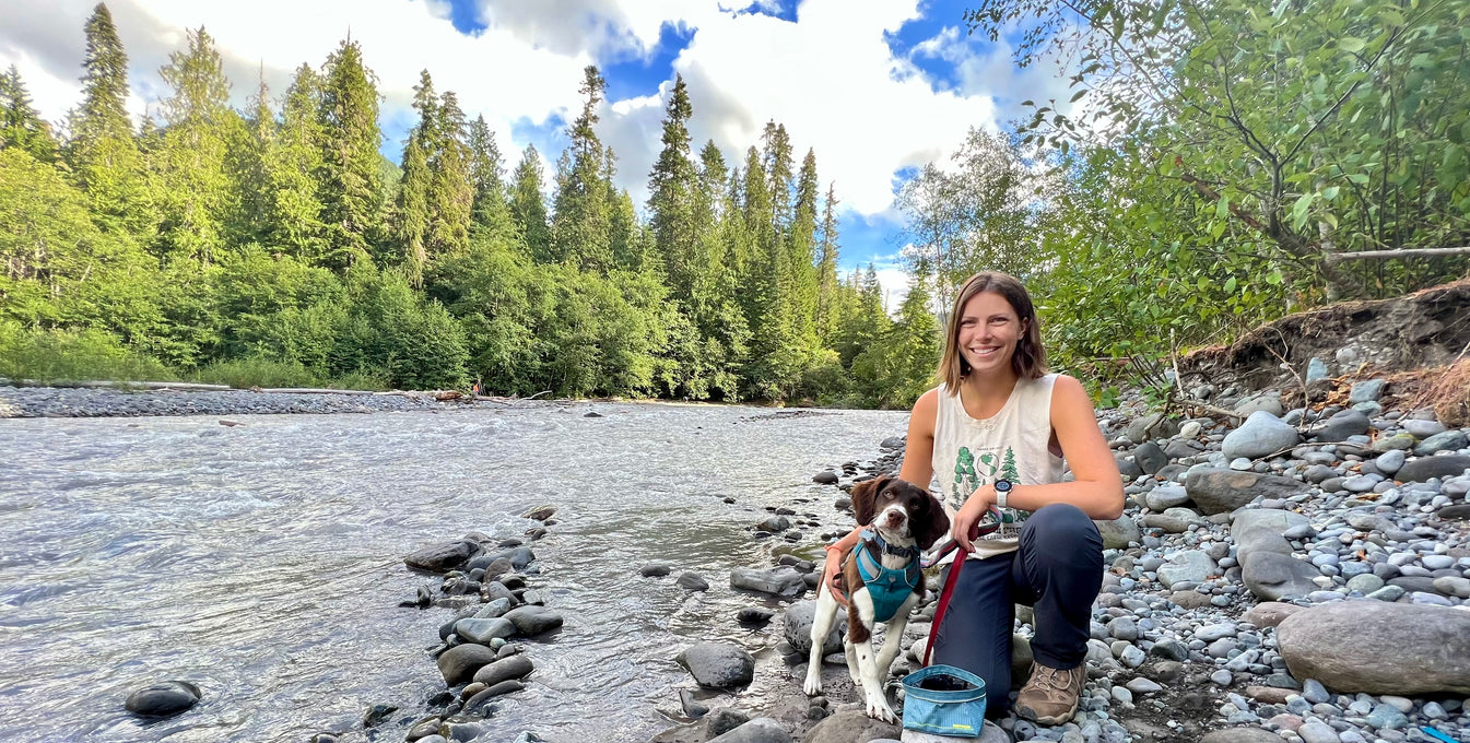 A woman sits by a lake with her puppy. 
