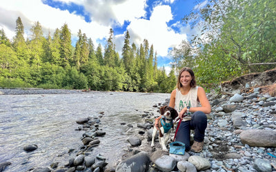 A woman sits by a lake with her puppy. 