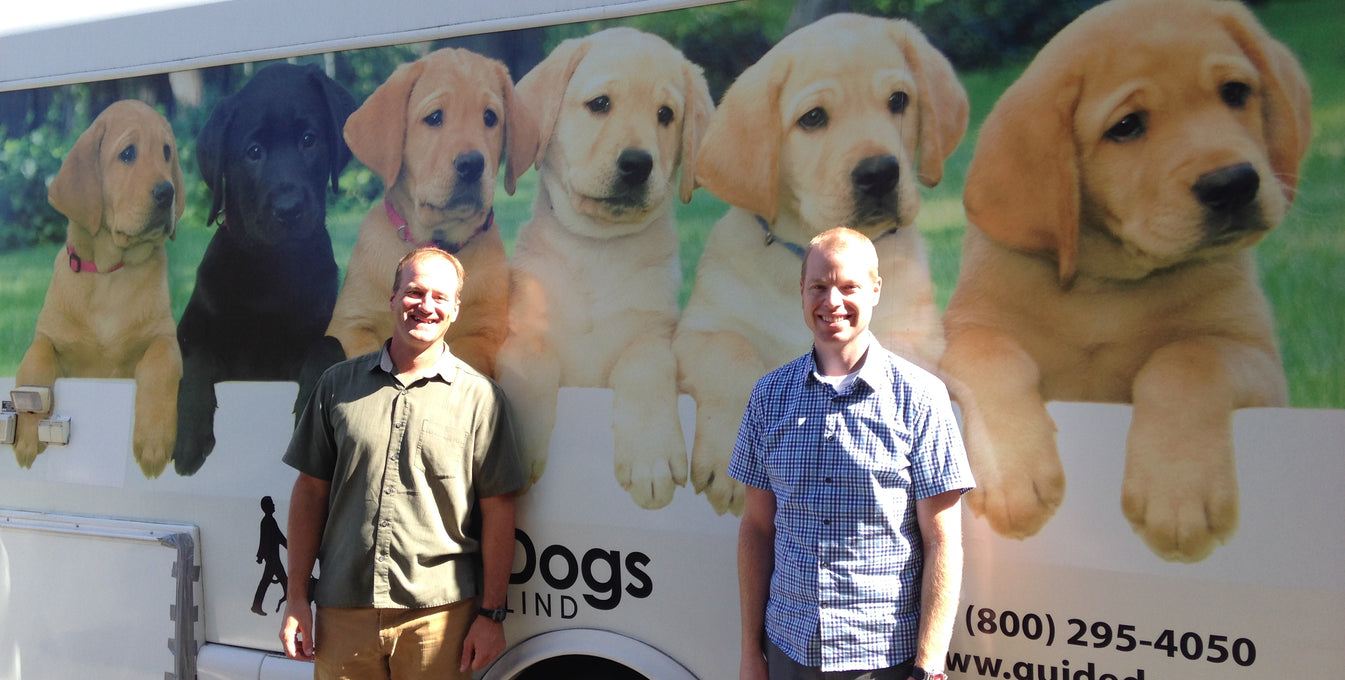 Two Ruffwear employees stand in front of a Guide Dogs for the Blind bus. 
