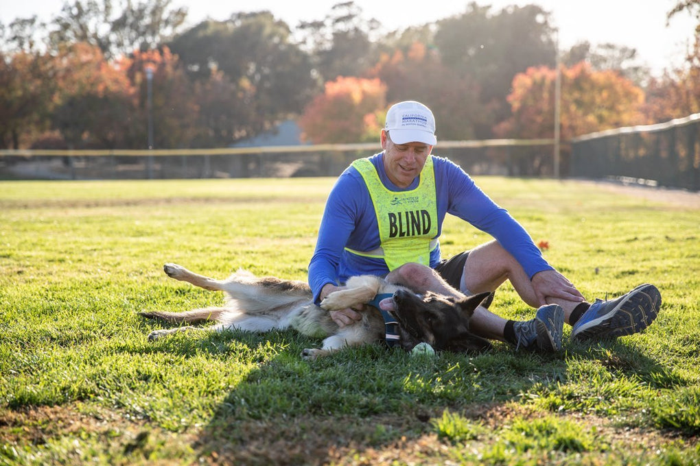 Klinger lays on his back next to Richard getting pet in a grass field.