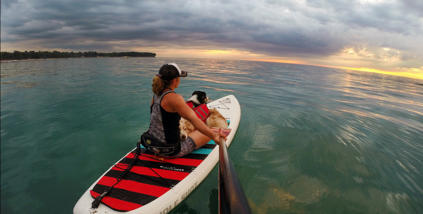 Maria on SUP with dogs in float coat dog life jackets on great lakes.