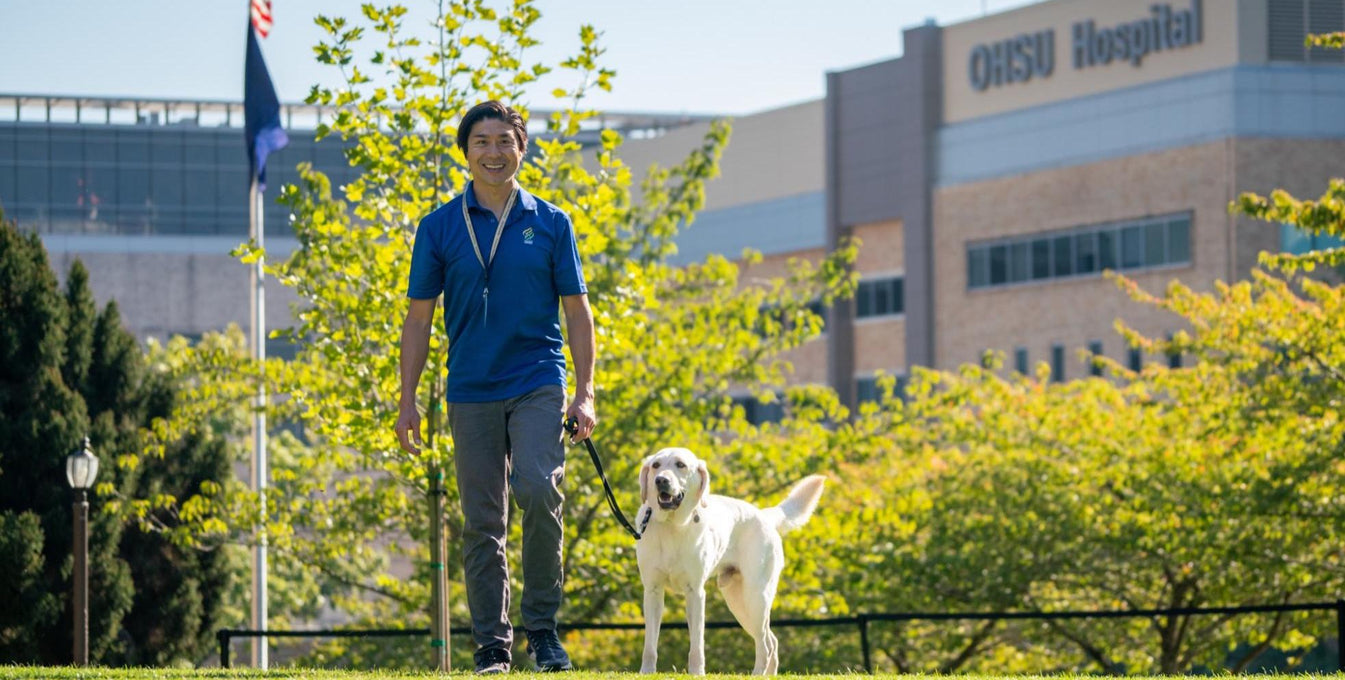 A man and his dog stand on the grass in front of OHSU Hospital. 