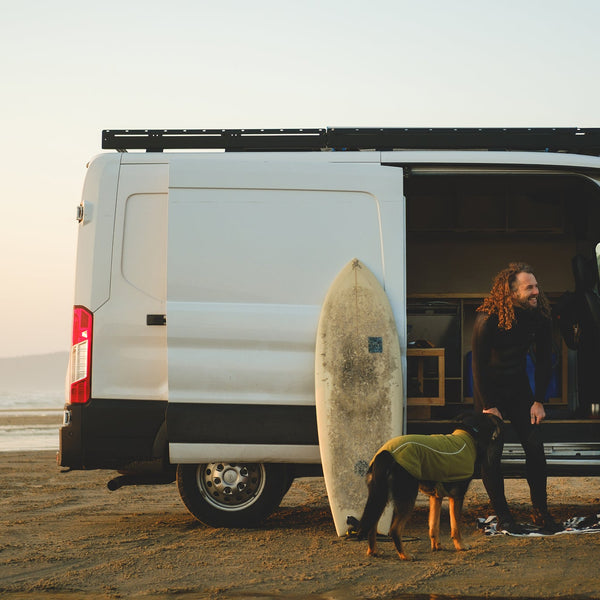 A man sits behind his truck with his dog on a bed