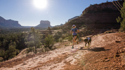 Woman trail runs with dog using cooling gear and dog boOTs for hot days.